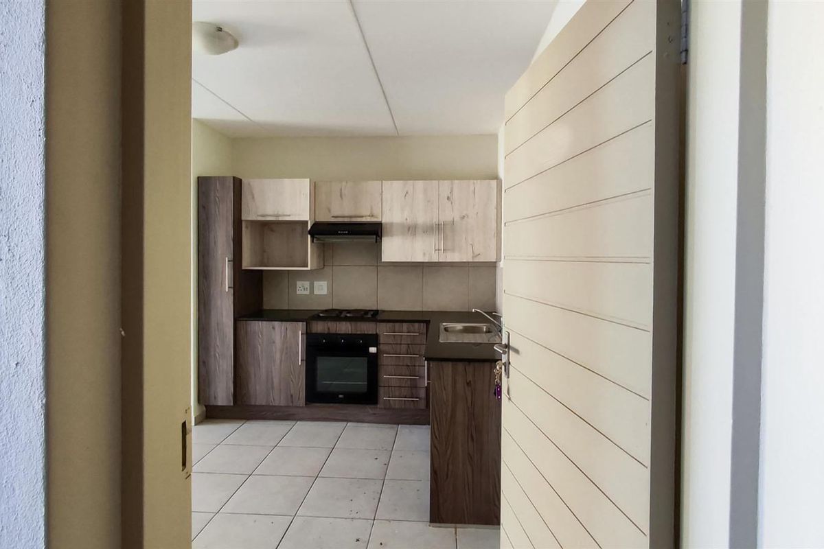 A functional kitchen featuring modern two-tone cabinetry, built-in oven, hob, extractor fan, and tiled flooring, presented in a clean, empty space.