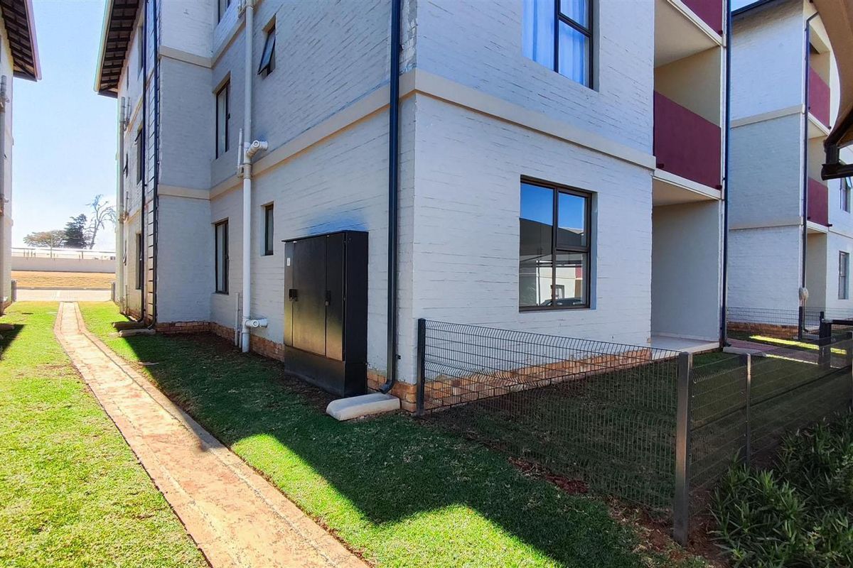 Exterior view of the apartment building showing the brick facade, paved walkway, and surrounding landscaped grounds.