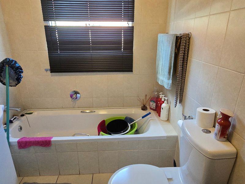 A functional bathroom featuring a bathtub, vanity basin, and toilet with neutral wall and floor tiling.
