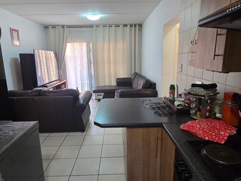 Open-plan living area featuring a functional kitchen with built-in cabinetry, electric hob, and extractor fan, flowing into a tiled lounge space with balcony access.