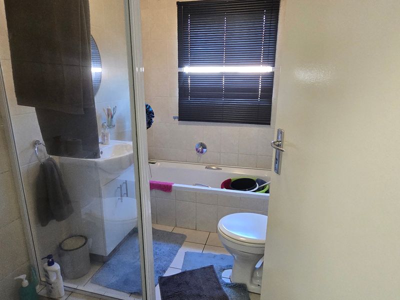 A functional bathroom featuring a shower enclosure, bathtub, vanity basin, and toilet with tiled finishes and a window blind.