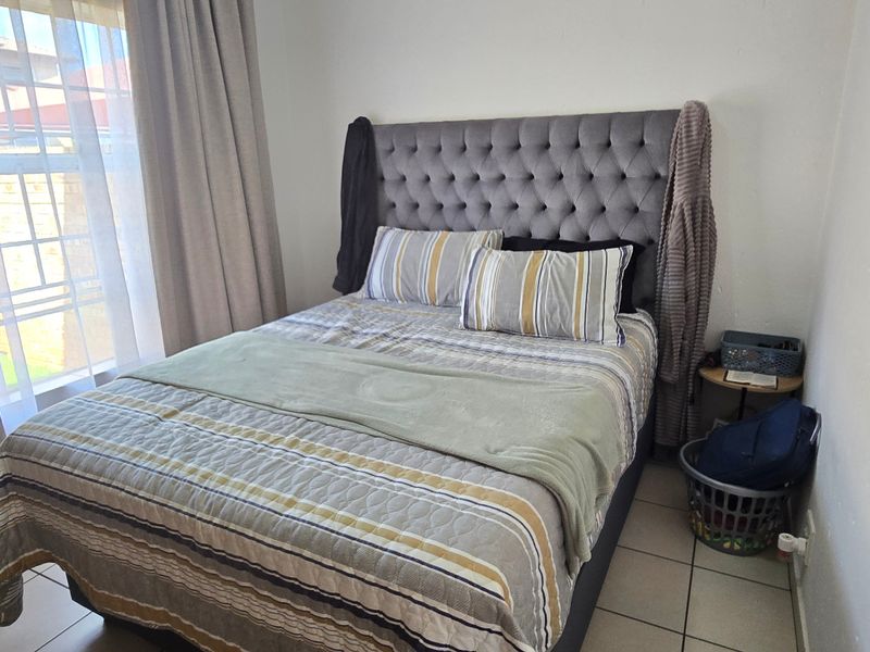 A compact bedroom featuring tiled flooring and large windows with curtain treatments, providing a functional and well-lit sleeping space.