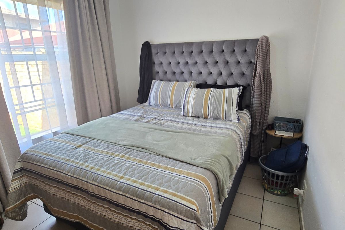 A compact bedroom featuring tiled flooring and large windows with curtain treatments, providing a functional and well-lit sleeping space.