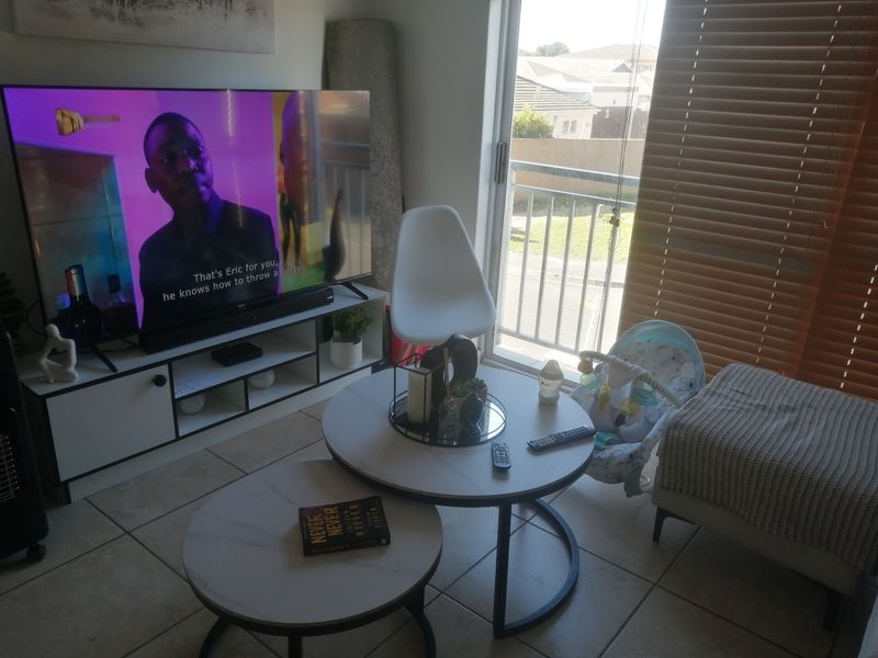 A living room area featuring tiled flooring, a sliding glass door leading to a balcony, and fitted venetian blinds.