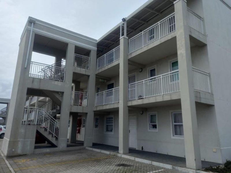Exterior view of a multi-story apartment building featuring concrete staircases, metal balustrades, and a paved parking area at the front entrance.