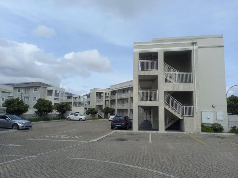 Exterior view of an apartment complex featuring a paved parking area and external stairwell access to the residential units.