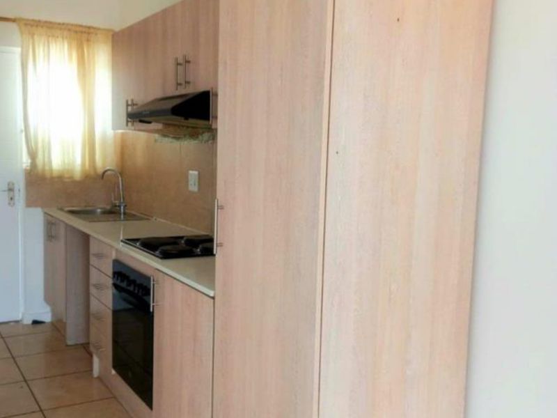 A functional kitchen featuring light wood-finish cabinetry, integrated appliances including an oven and hob, and tiled flooring.