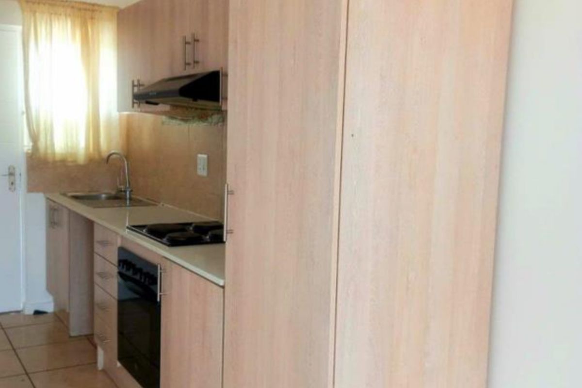 A functional kitchen featuring light wood-finish cabinetry, integrated appliances including an oven and hob, and tiled flooring.