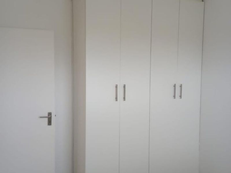 A clean, empty bedroom featuring neutral laminate flooring and a large, white built-in wardrobe with modern handles.