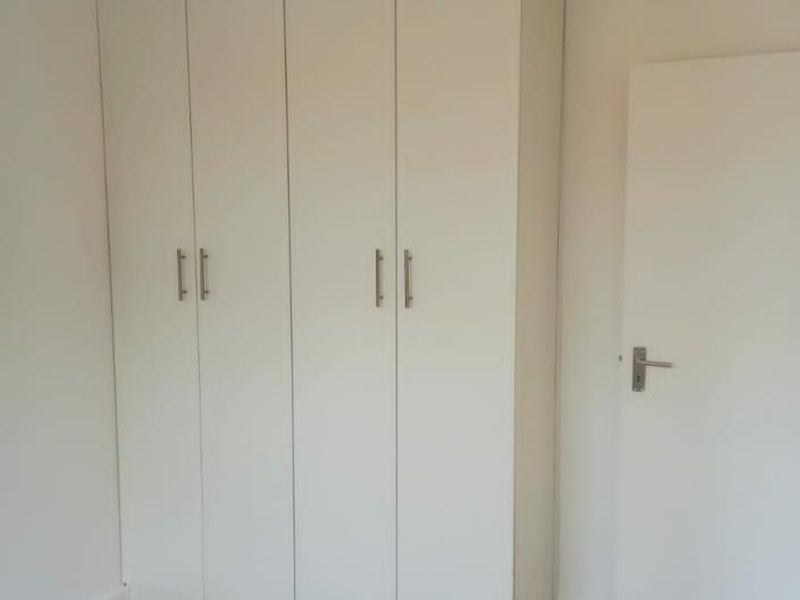 A clean, empty bedroom featuring neutral laminate flooring and a large, white built-in wardrobe with modern handles.