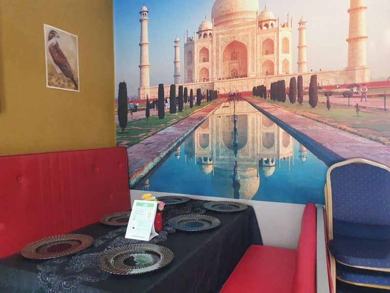 A dining area featuring a large wall mural of the Taj Mahal, red booth seating, and a table set for dining.