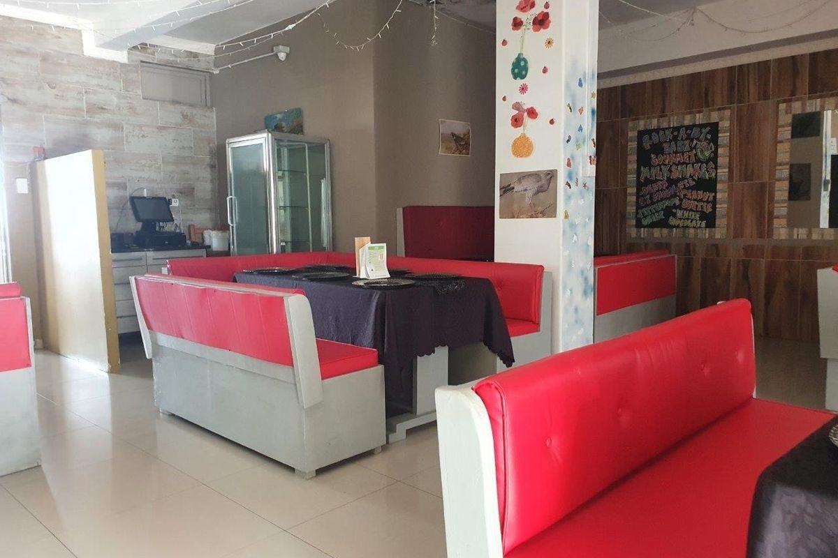 Commercial dining area featuring built-in booth seating, tiled flooring, and wood-look wall paneling, with visible water damage on the ceiling.