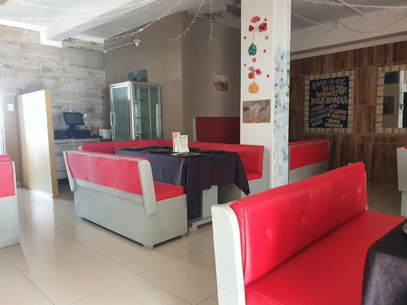 Commercial dining area featuring built-in booth seating, tiled flooring, and wood-look wall paneling, with visible water damage on the ceiling.