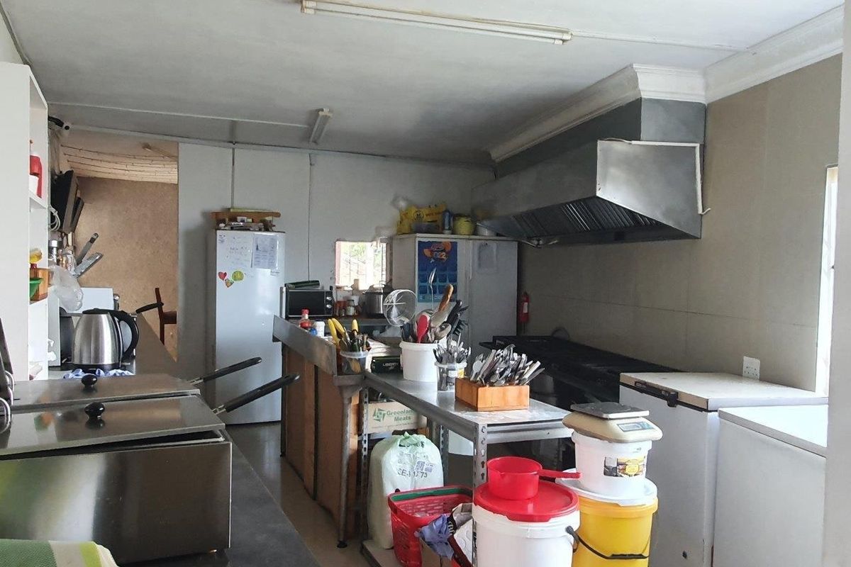 Commercial kitchen space featuring a stainless steel extractor hood, tiled splashbacks, and functional layout suitable for food preparation and service.