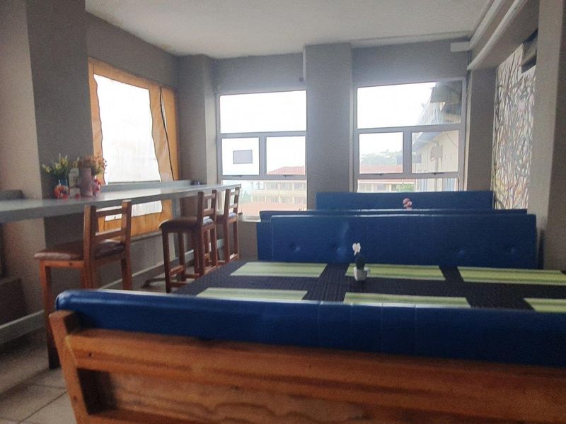 Open plan commercial dining area featuring large windows, built-in bar seating, and tiled flooring, suitable for a restaurant or cafe setting.