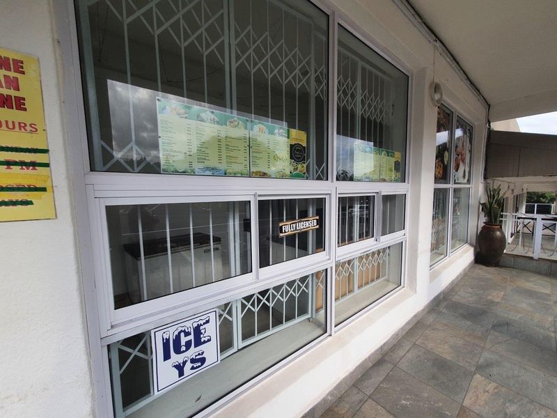 Commercial storefront exterior featuring aluminium window frames with security gates and a covered tiled walkway.