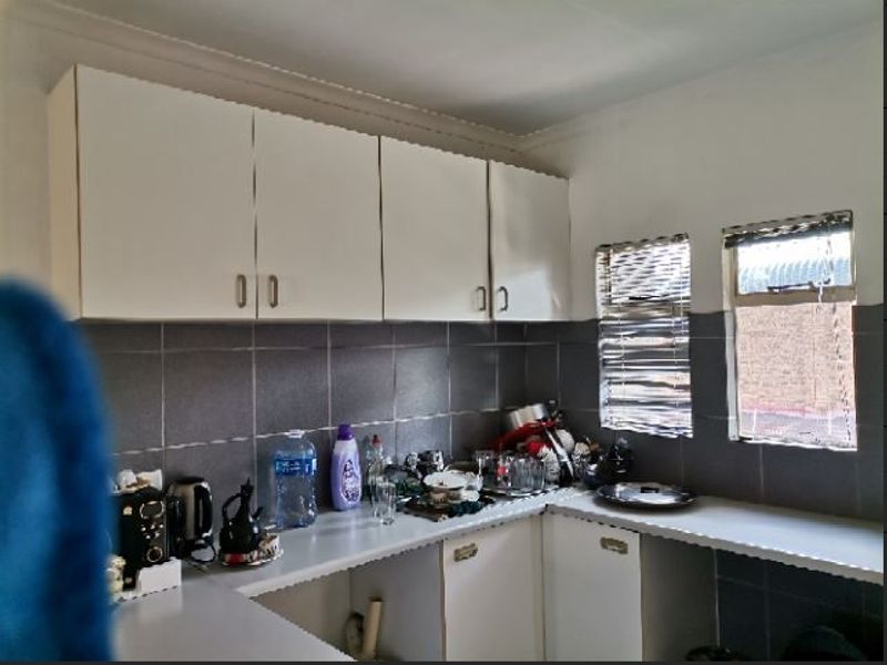 A functional kitchen area featuring built-in cabinetry, laminate countertops, and a tiled backsplash with natural light from two windows.