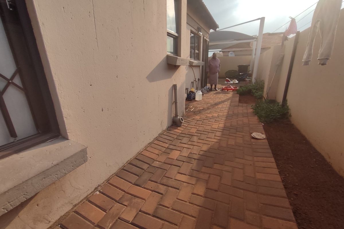 A side exterior view of the property featuring a paved walkway, perimeter wall with security fencing, and external lighting.