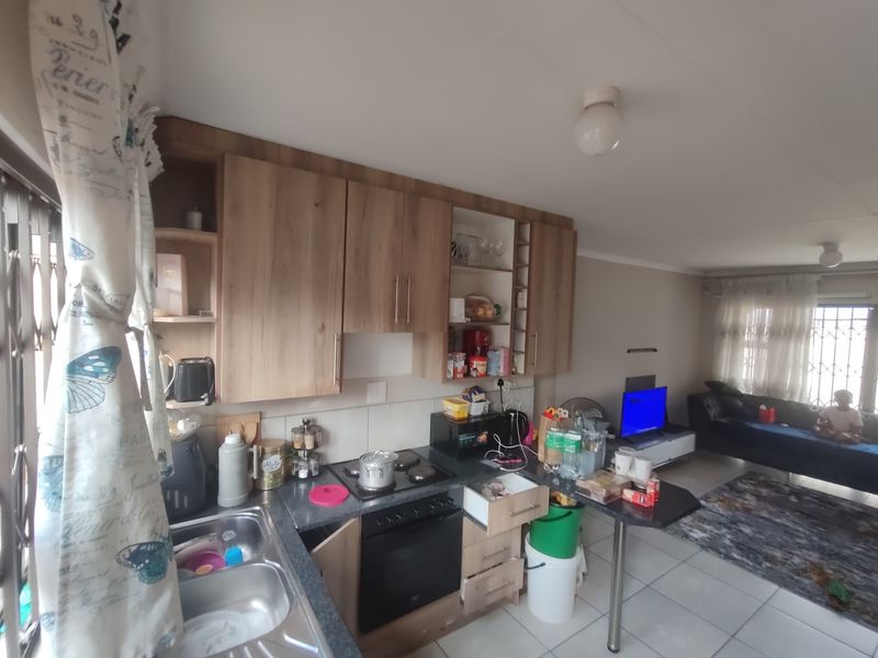 Open-plan kitchen and living area featuring wood-look cabinetry, built-in oven and hob, and tiled flooring throughout.