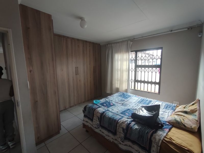 A functional bedroom featuring built-in wooden cupboards, tiled flooring, and a window fitted with a security gate.