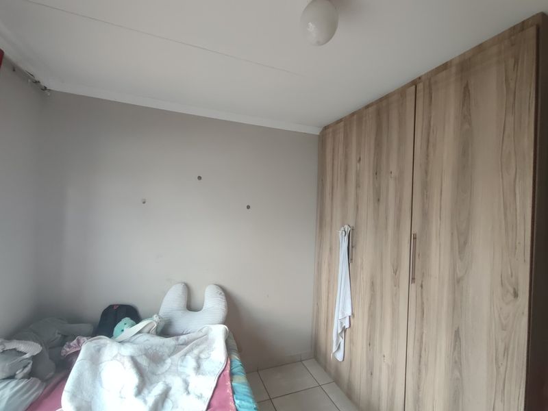 A bedroom featuring light-toned tiled flooring and a large, modern wood-finish built-in wardrobe providing ample storage space.