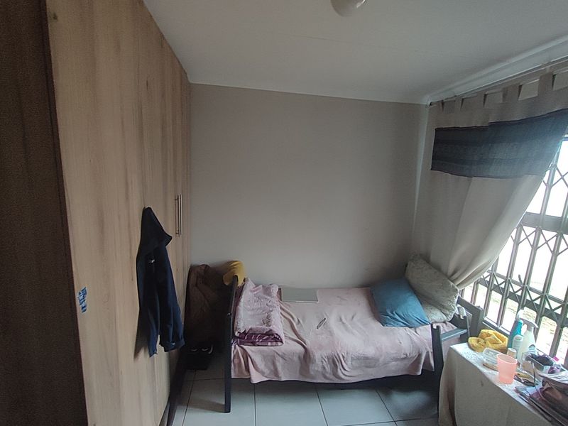 A functional bedroom featuring built-in wardrobes, tiled flooring, and a security gate on the window.