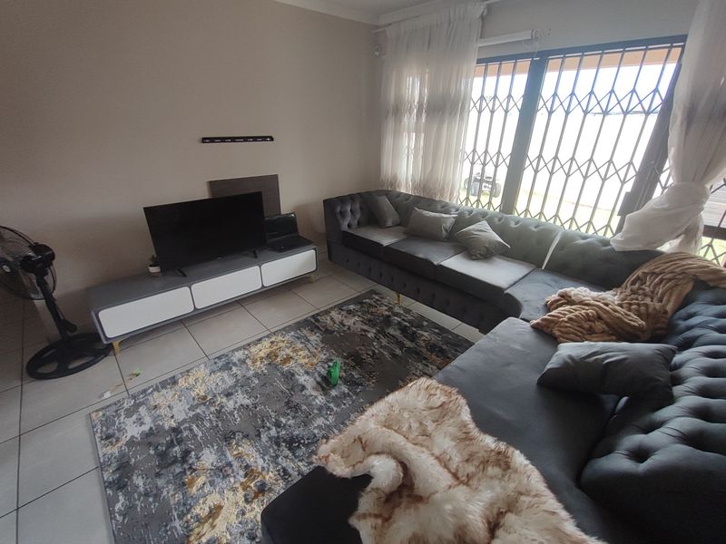 A living room featuring tiled flooring and large windows fitted with security gates and curtain rails.