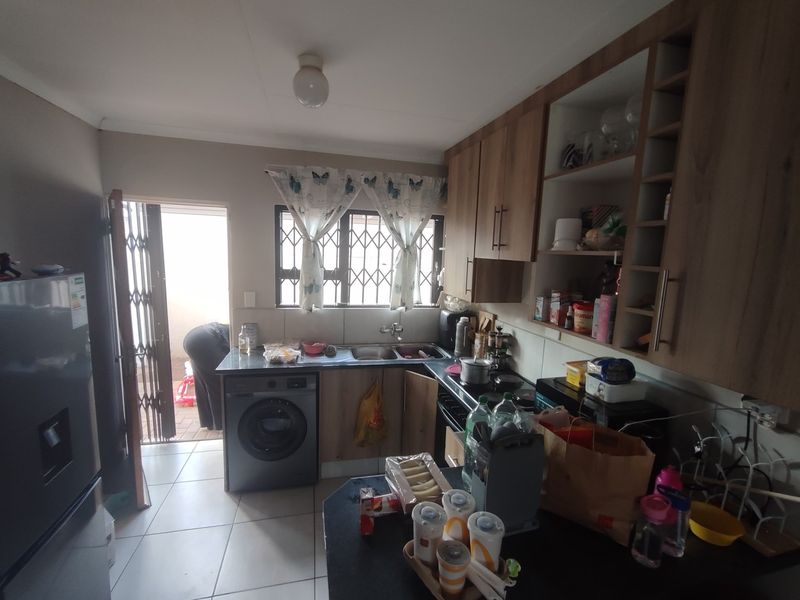 Functional kitchen featuring wood-look cabinetry, laminate countertops, tiled flooring, and direct access to an exterior area via a security gate.
