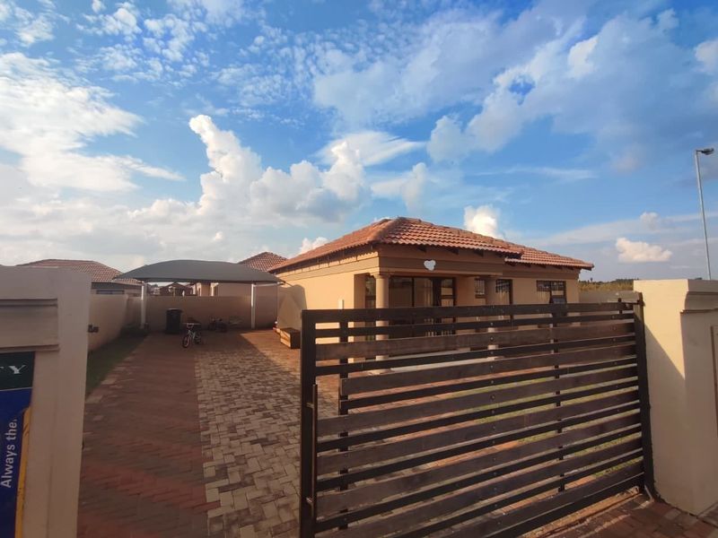 Front view of a residential property featuring a paved driveway, carport, and secure boundary wall with a slatted gate.