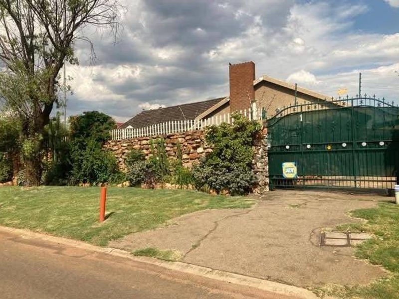 Front exterior view of the property featuring a stone boundary wall, metal security gate, brick chimney, and established garden area.