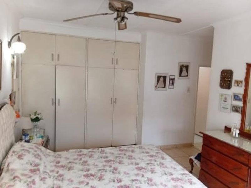 A bedroom featuring built-in cupboards, a ceiling fan, and tiled flooring, offering a functional space with potential for modern updates.