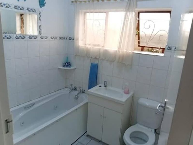 A functional bathroom featuring a bathtub, vanity basin, and toilet with tiled wall finishes and security bars on the windows.