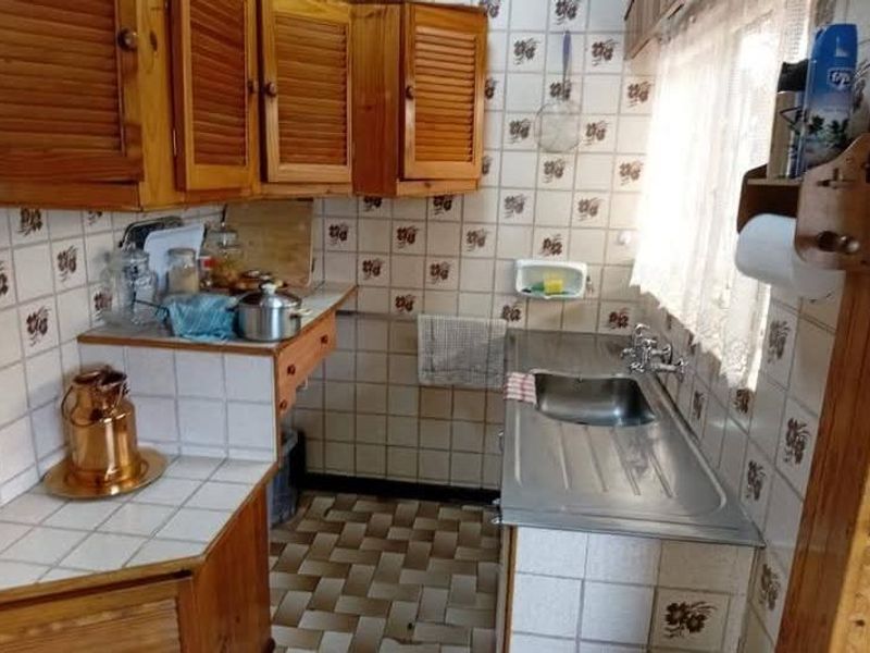 A compact kitchen featuring wooden cabinetry, tiled wall finishes, and a stainless steel sink with a window view.
