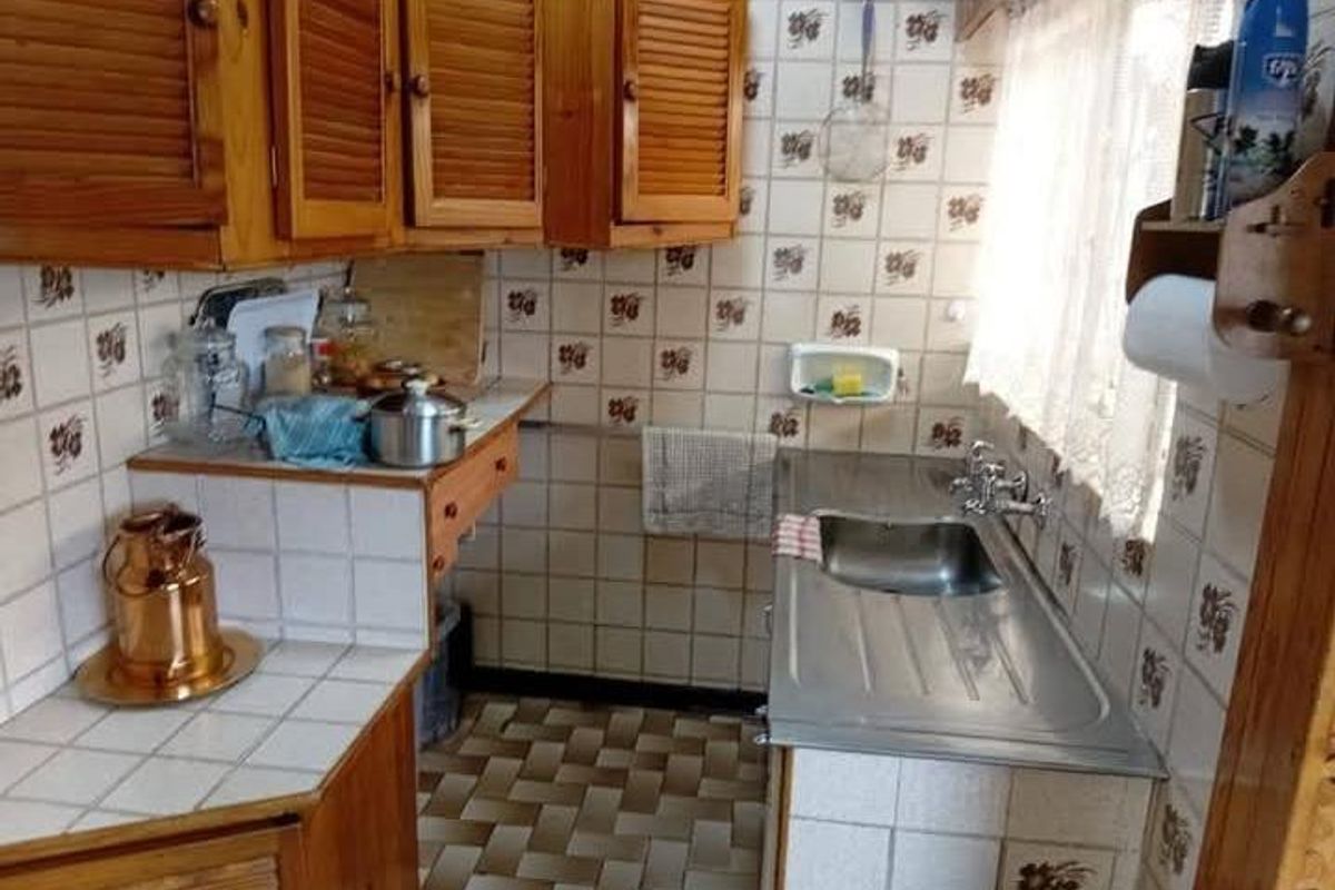 A compact kitchen featuring wooden cabinetry, tiled wall finishes, and a stainless steel sink with a window view.
