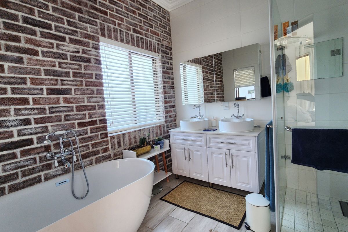 Modern bathroom featuring a freestanding bathtub, double vanity with vessel sinks, walk-in shower, and a stylish exposed brick feature wall.