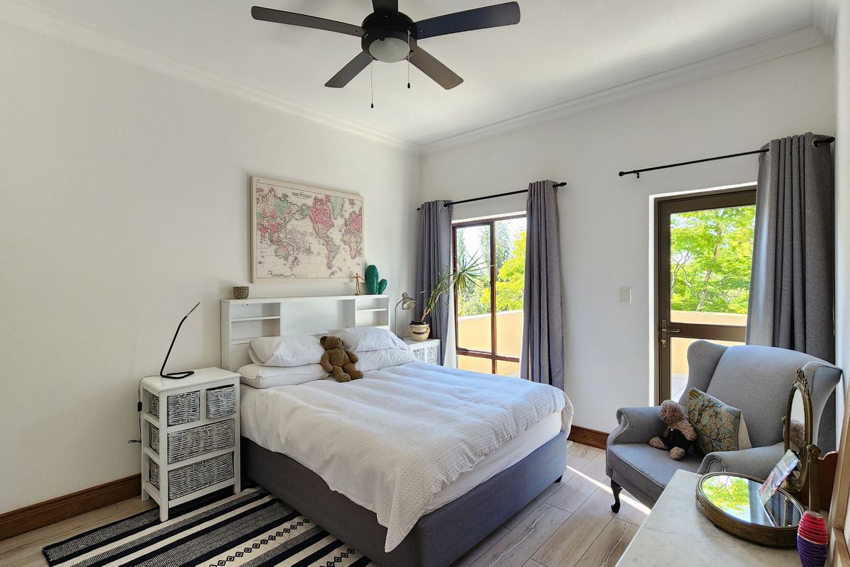 A bright and well-maintained bedroom featuring tiled flooring, a ceiling fan, built-in cupboards, and direct access to an outdoor balcony through a sliding door.