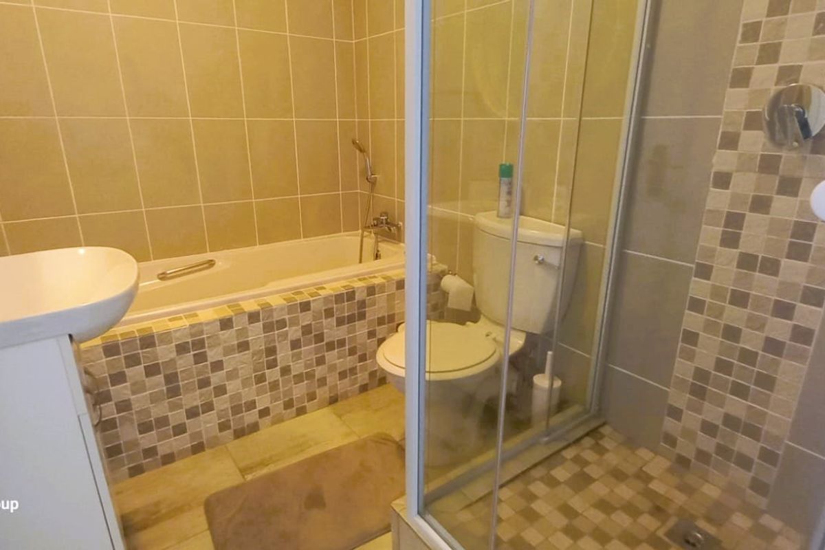 A functional bathroom featuring a separate bathtub and shower enclosure with neutral tiled finishes and a pedestal basin.