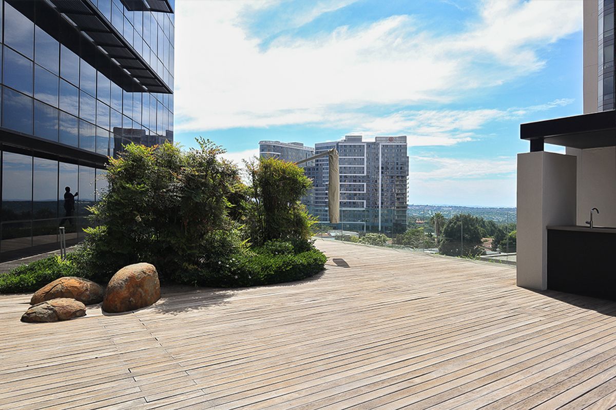 Spacious outdoor terrace featuring timber decking, a built-in sink, and glass balustrades with expansive urban views.