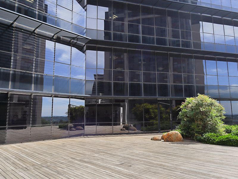 A modern commercial outdoor terrace featuring timber decking and a glass curtain wall facade with integrated landscaping.