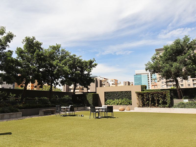 A well-maintained commercial garden area featuring artificial turf, landscaped hedges, and a decorative feature wall, providing a pleasant outdoor space.
