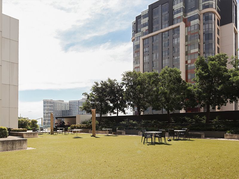 A spacious outdoor terrace featuring artificial turf, landscaped trees, and built-in concrete seating, providing a pleasant communal area within the commercial complex.