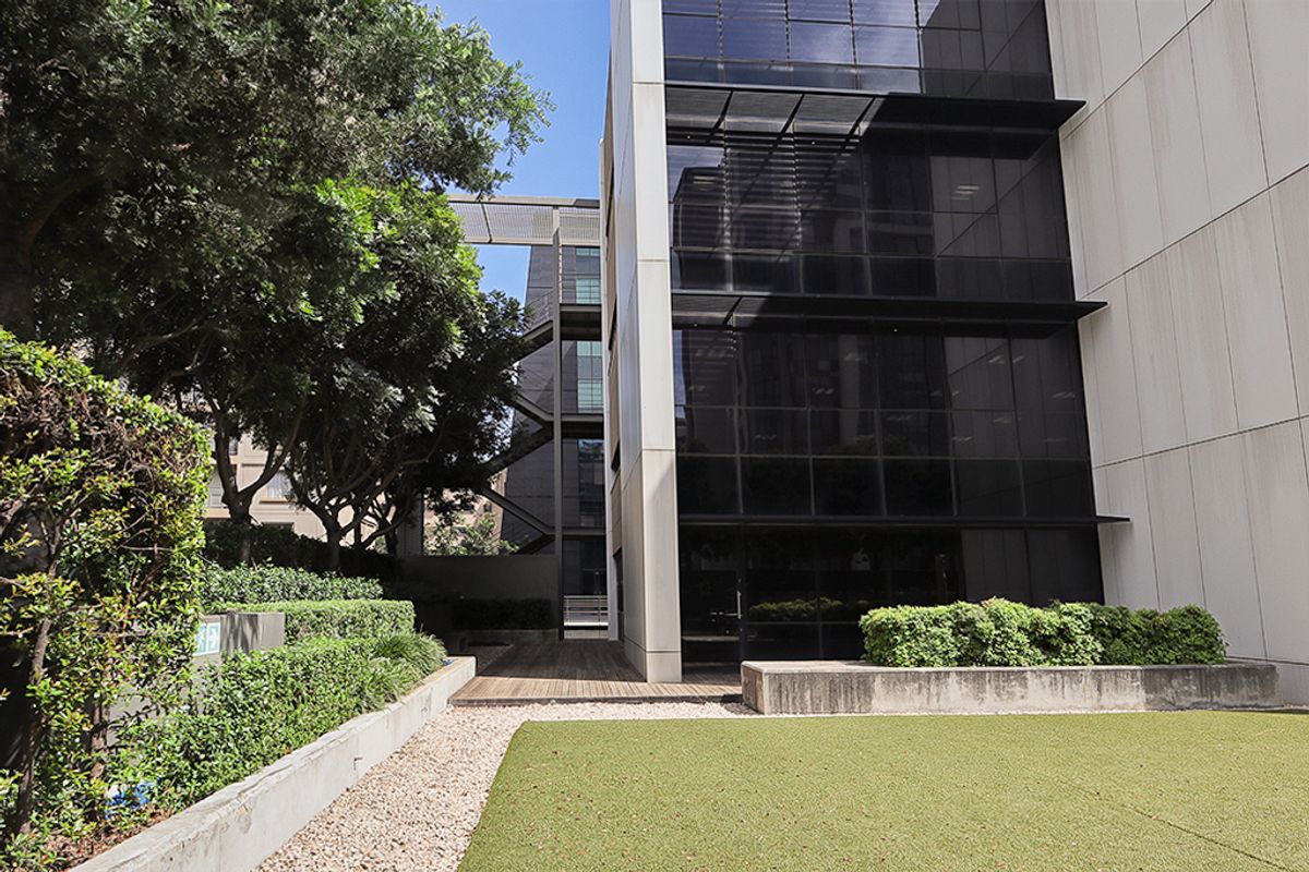 Modern commercial building exterior featuring a glass facade, metal fire escape, timber decking, and landscaped garden area.