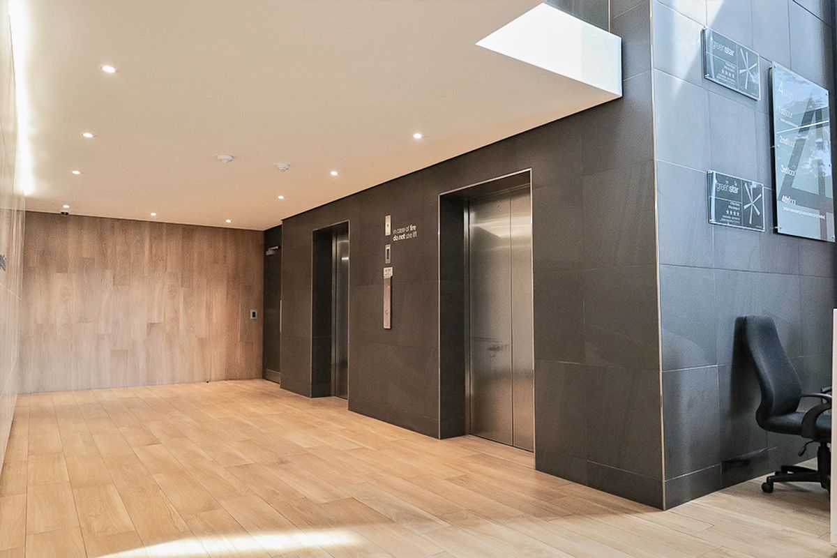 Modern commercial building lobby featuring stainless steel elevator banks, high-quality stone and wood wall finishes, and recessed ceiling lighting.