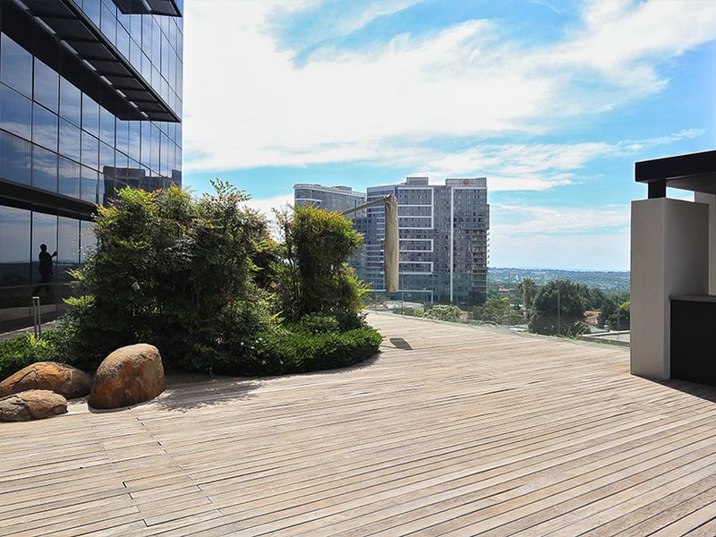 Spacious outdoor terrace featuring timber decking, a built-in sink, and glass balustrades with expansive urban views.