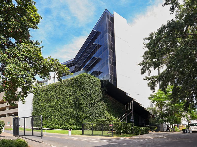 Modern commercial building facade featuring a glass curtain wall, integrated vertical garden, and secure gated entrance with paved driveway access.
