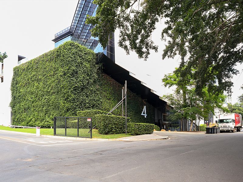 Modern commercial building exterior featuring a prominent green wall, glass facade, and well-maintained landscaping at the street-level entrance.