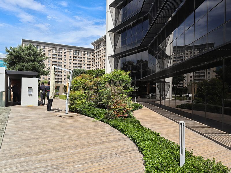 Modern commercial terrace featuring timber decking, glass balustrades, and landscaped garden beds adjacent to a contemporary glass-facade office building.