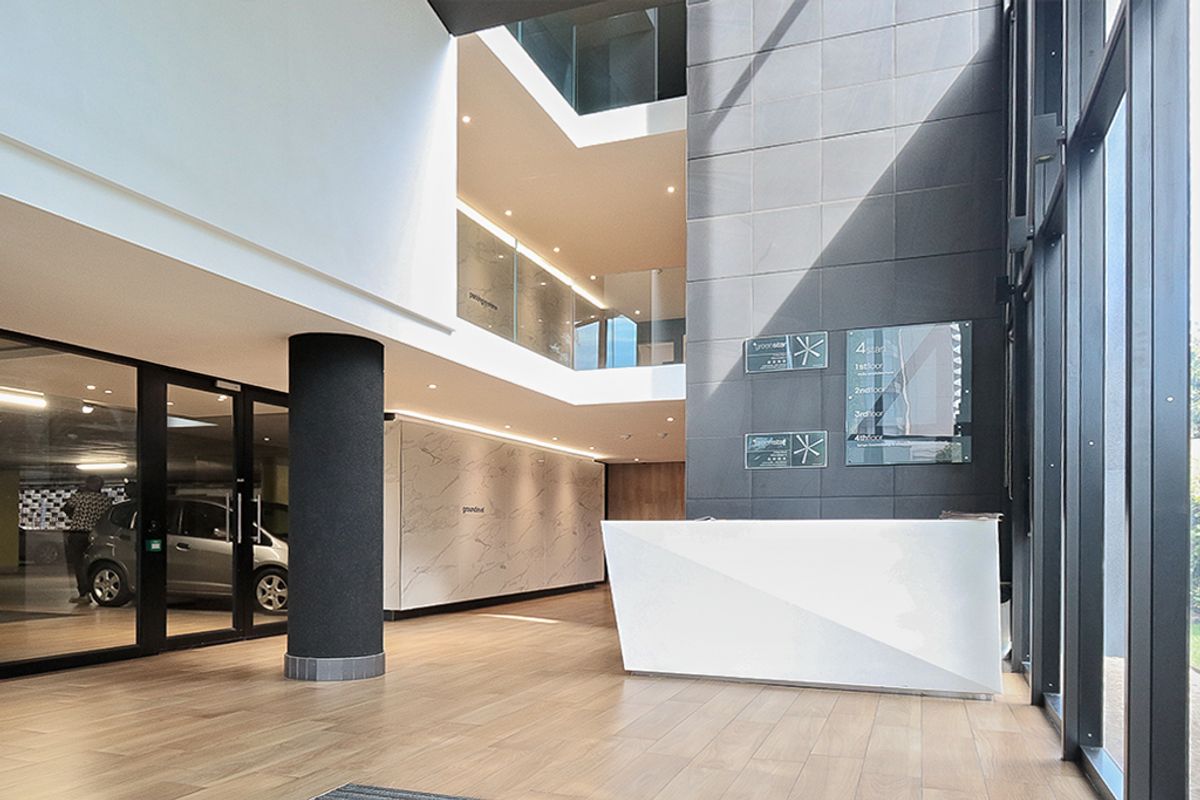 Modern commercial building lobby featuring a sleek reception desk, floor-to-ceiling glass windows, marble-look wall finishes, and a multi-level atrium design.