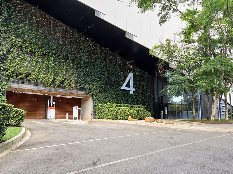 Modern commercial building entrance featuring a vertical garden, glass facade, and secure boom gate access with paved driveway.