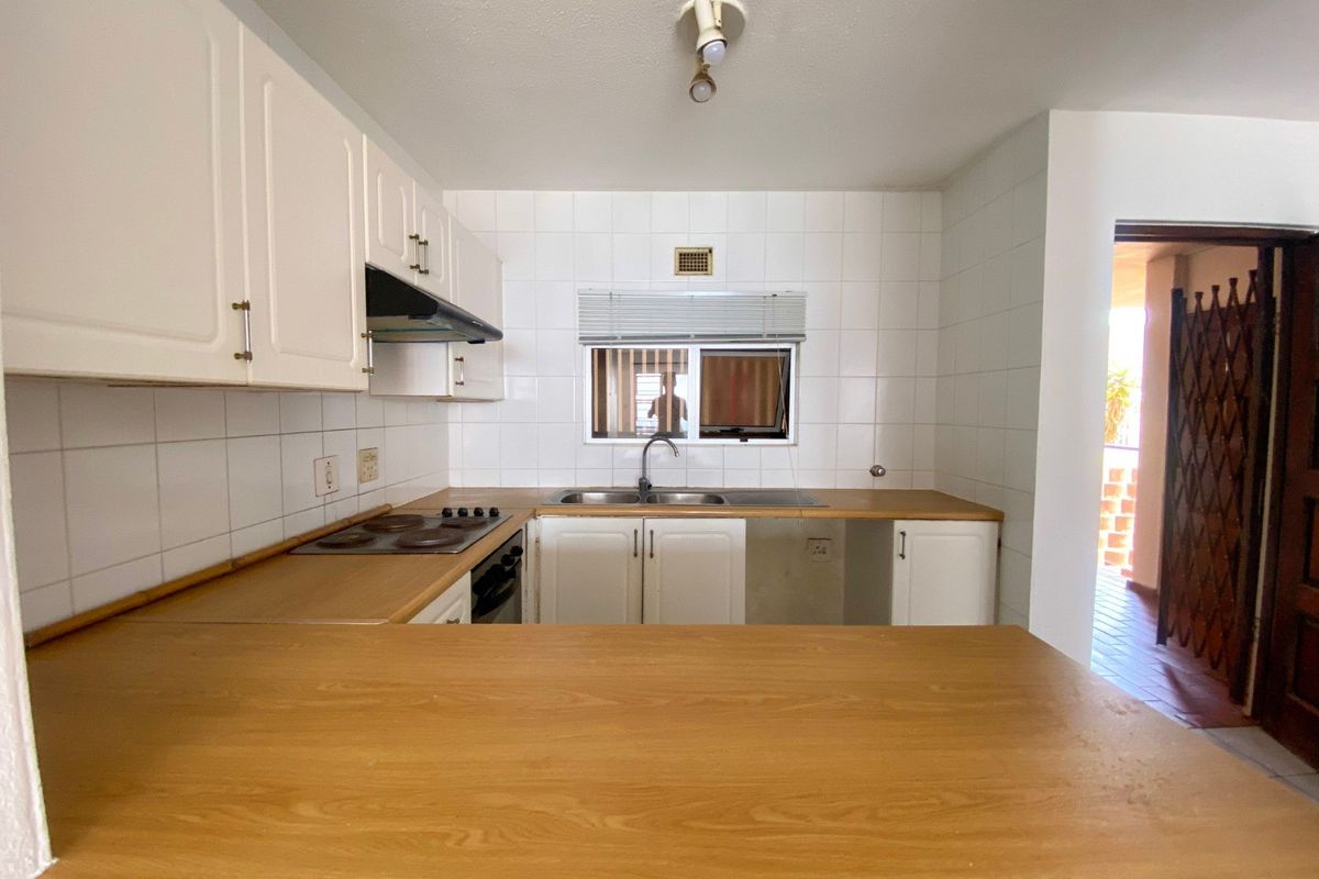 A functional kitchen featuring white cabinetry, laminate countertops, an electric hob, and a double sink, with an adjacent doorway leading to an outdoor area.